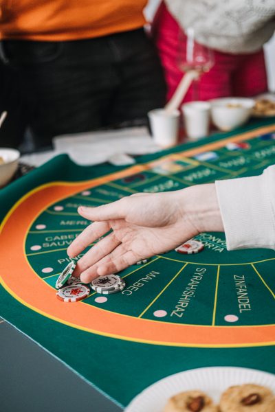 Hands playing at a wine-themed casino game, with glasses of rose in the background, blending gambling and wine tasting Hands playing at a wine-themed casino game, with glasses of rose in the background, blending gambling and wine tasting